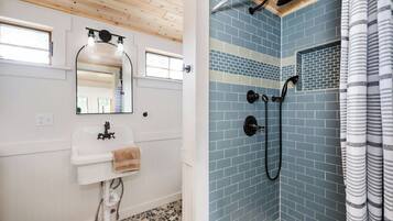 A bathroom with a white sink, mirror, and tiled shower area.