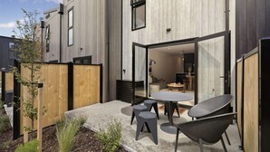 Ein modernes Gebäude mit einer Terrassenfläche, komplett mit Tisch und Stühlen, einem Holzzaun und einem kleinen Garten.