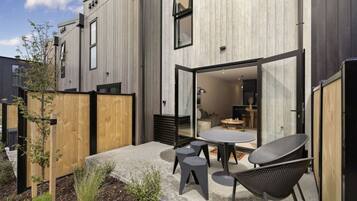 A modern building with a patio area featuring a table and chairs, a wooden fence, and a small garden.