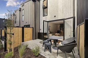 Een modern gebouw met een terras, een tafel en stoelen, een houten schutting en een kleine tuin.