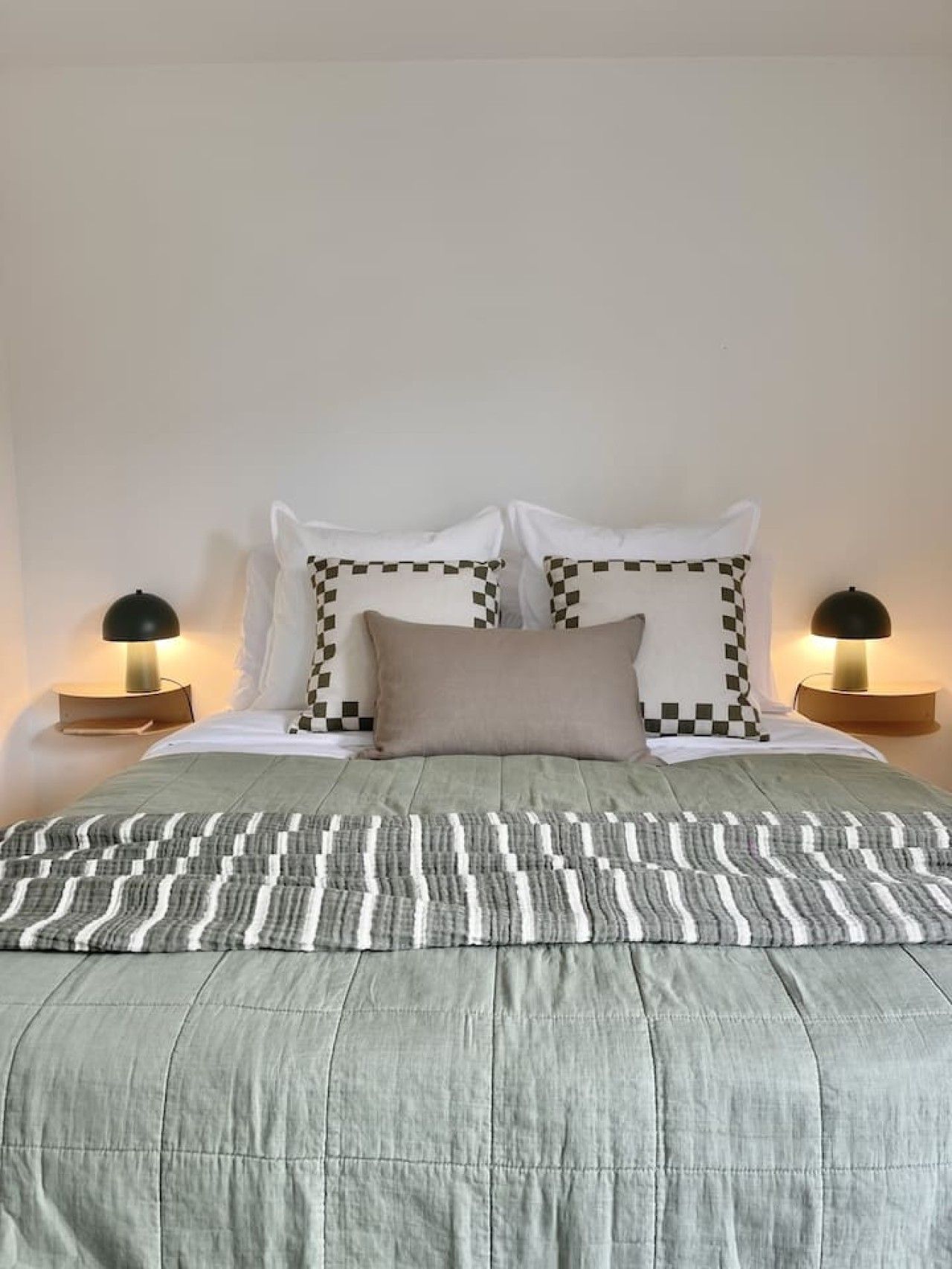 Uma cama com colcha estampada, duas luminárias de cabeceira e dois travesseiros com padrão xadrez.