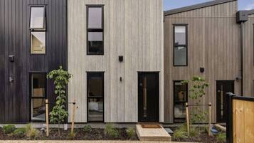 Un moderno edificio residencial de varios pisos con techo plano, grandes ventanales y un pequeño jardín delantero.