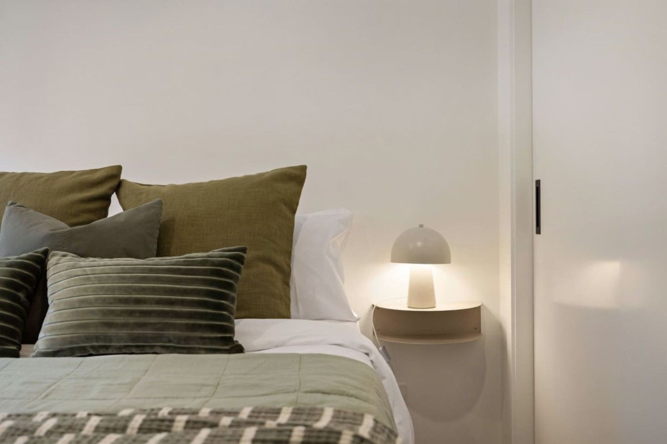 A bedroom with a bed, pillows, a bedside lamp, and a nightstand.
