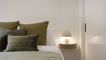 A bedroom with a bed, pillows, a bedside lamp, and a nightstand.