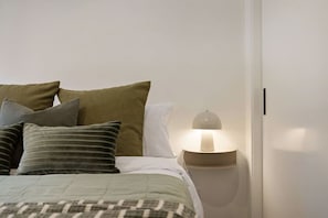 Een slaapkamer met een bed, kussens, een bedlampje en een nachtkastje.