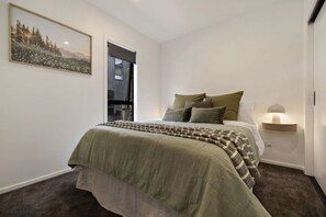 A bedroom with a bed, pillows, a bedside lamp, a wall-mounted shelf, and a framed picture. - Kawarau Retreat, Queenstown (Queenstown)