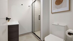 Ein modernes Badezimmer mit Duschkabine aus Glas, einer weißen Toilette und einem gerahmten abstrakten Kunstwerk an der Wand.