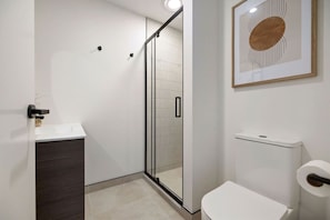 Een moderne badkamer met een douchecabine van glas, een wit toilet en een abstract kunstwerk in een lijst aan de muur.