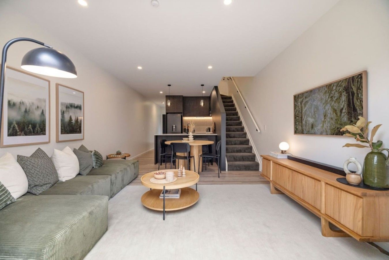 A modern living room with a sofa, a coffee table, and a dining area with chairs. There is a staircase leading to an upper level.