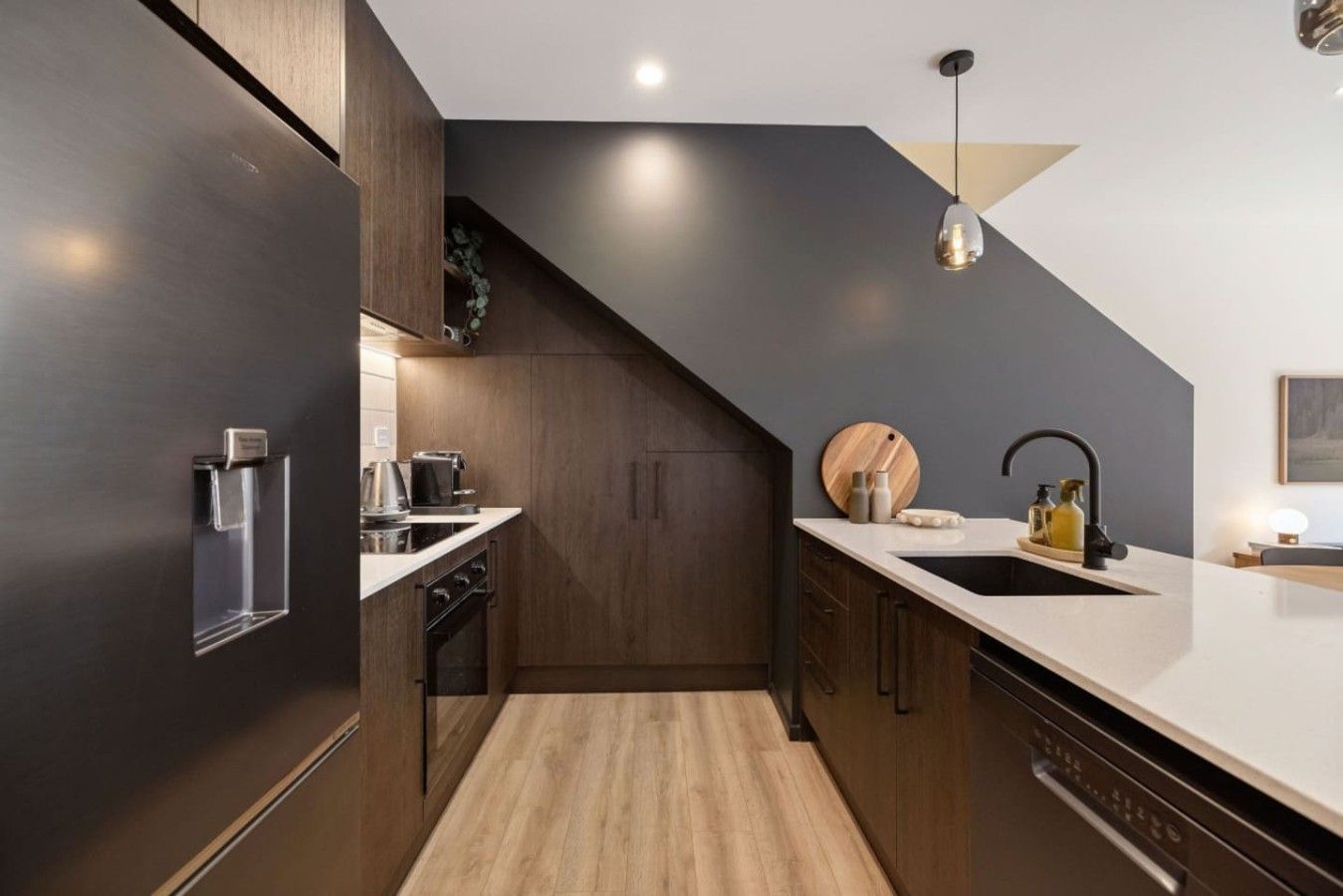 Une cuisine moderne avec des meubles de couleur sombre, un plan de travail en bois, un four encastré et un évier doté d’un robinet noir.