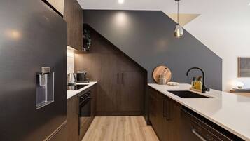 Une cuisine moderne avec des meubles de couleur sombre, un plan de travail en bois, un four encastré et un évier doté d’un robinet noir.
