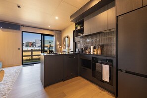 A modern kitchen with dark cabinetry, a built-in oven, and a large window overlooking a grassy area. - Prime Location Luxury Villa (Queenstown)