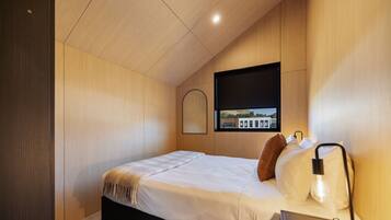 Quarto moderno com cama, abajur, janela com vista e televisão na parede.