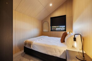 A modern bedroom with a bed, a bedside lamp, a window with a view, and a mounted TV. - Prime Location Luxury Villa (Queenstown)