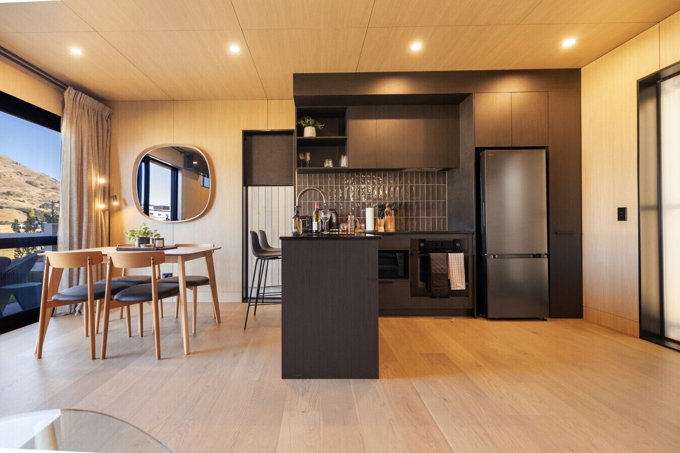 A modern kitchen with a central island, dark cabinetry, and a built-in oven.