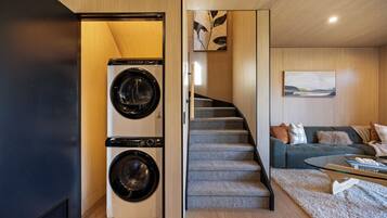 A modern interior with a dual washing machine, a staircase, and a living area with a sofa and cushions.