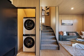 A modern interior with a dual washing machine, a staircase, and a living area with a sofa and cushions. - Prime Location Luxury Villa (Queenstown)