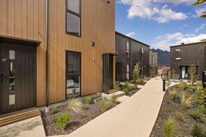 A modern residential building with a central walkway, wooden exterior, and small landscaped areas. - Prime Location with Mountain Views (Queenstown)