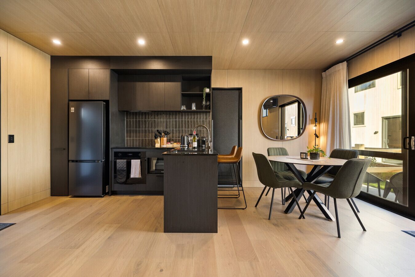A modern kitchen with a central island, dining area with chairs, and a large window with curtains.