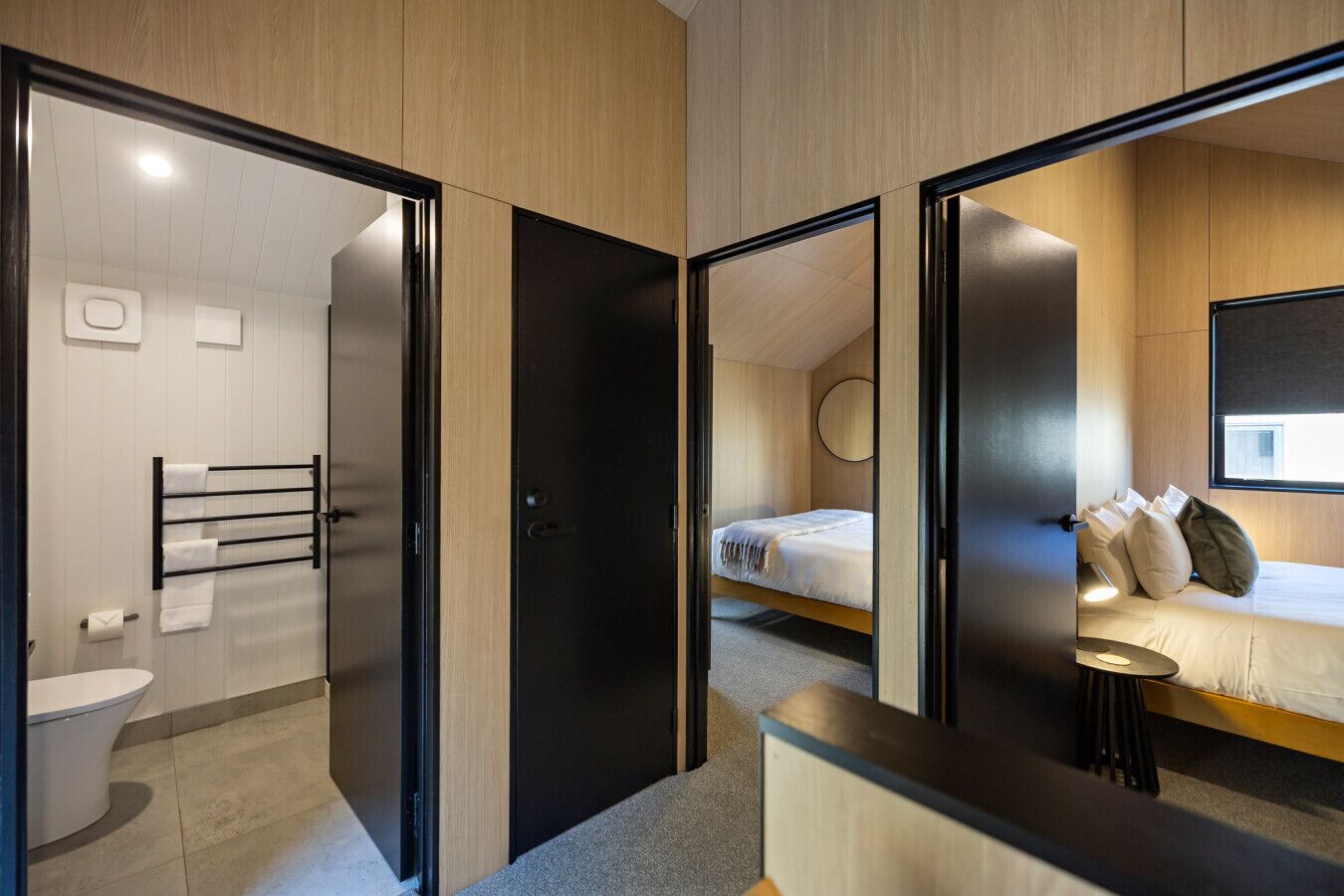 A modern hotel room with a bathroom, a bed with pillows, a bedside table, and a mirror.
