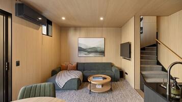A modern living room with a sofa, a coffee table, a TV mounted on the wall, and a staircase.