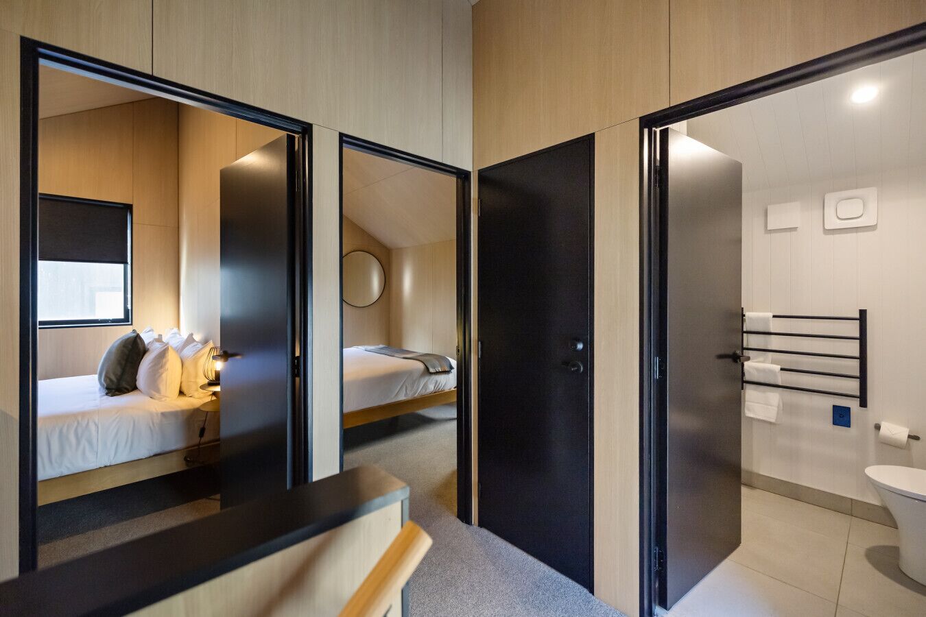 A modern hotel room with a bed, a desk, a mirror, and a bathroom with a toilet and towel rack.