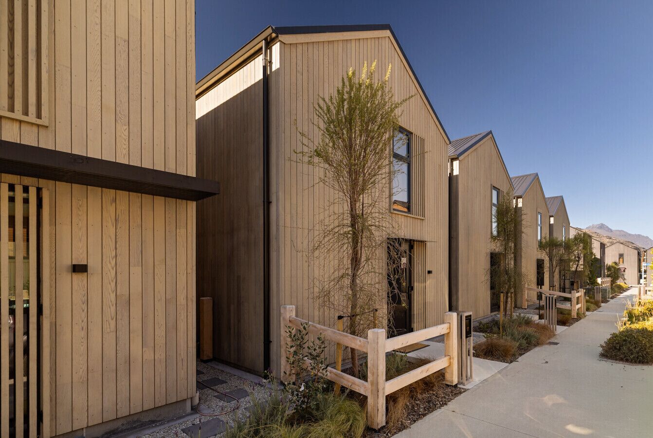 A row of modern wooden buildings with a gated entrance, a clear sky, and a well-maintained pathway.