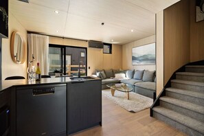 A modern kitchen with a built-in dishwasher, a dining area with a glass table, a gray sofa, and a staircase. - Luxury Queenstown 2Bed Villa (Queenstown)