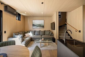 Un intérieur moderne comprenant un canapé d’angle, une table basse en verre, un coin cuisine avec un évier et un escalier.