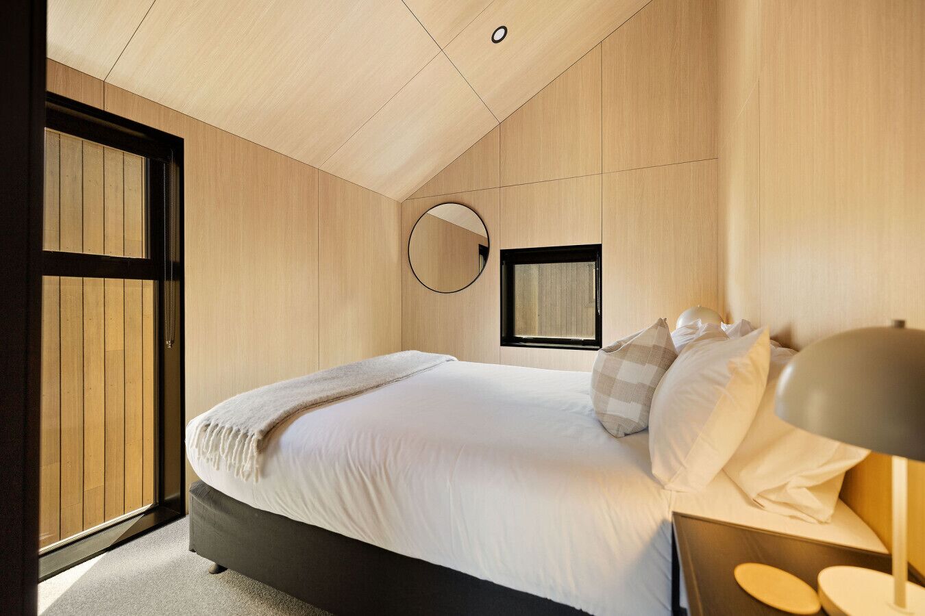 A bedroom with a bed, a bedside table, a lamp, and a window.