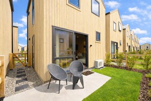 Ein modernes Gebäude mit Holzfassade, großen Fenstern und einer Terrasse mit Sitzgelegenheiten.
