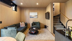 A modern living room with a sofa, a coffee table, a painting on the wall, a TV, and a staircase. - Luxury Queenstown 2Bed Villa (Queenstown)