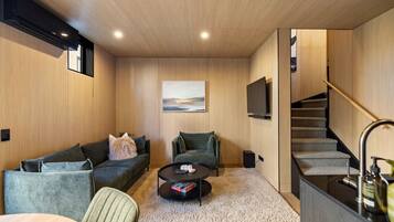 A modern living room with a sofa, a coffee table, a painting on the wall, a TV, and a staircase.