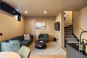 Ein modernes Wohnzimmer mit einer Couch, einem Couchtisch, einem Bild an der Wand, einem Fernseher und einer Treppe.