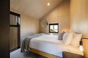 Ein Schlafzimmer mit einem Bett, einer Nachttischlampe, einem Fenster und einem Spiegel an der Wand.