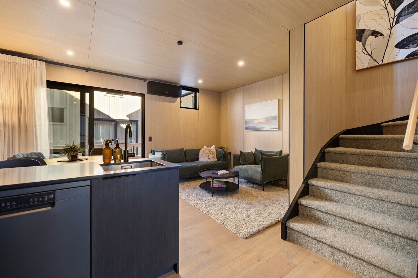 Una cocina moderna con una isla integrada, un comedor con mesa y sillas, una sala de estar con sofá y mesa de centro, y una escalera.