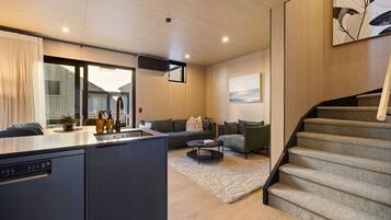 Una cocina moderna con una isla integrada, un comedor con mesa y sillas, una sala de estar con sofá y mesa de centro, y una escalera.