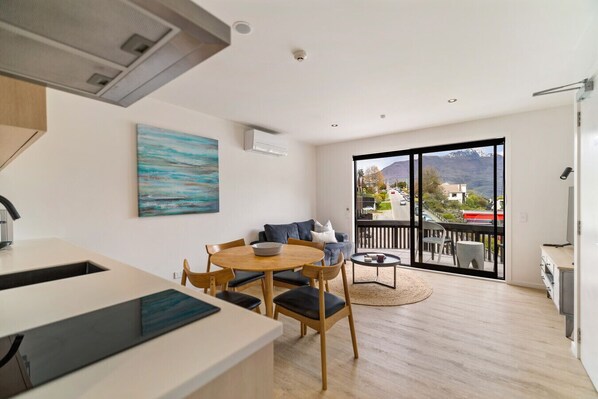 A modern kitchen with a dining area, a large window with a mountain view, and a balcony with outdoor seating. - Lake and Mountain Views (Queenstown)