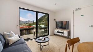 En moderne stue med en stor skydedør, der fører til en balkon, et fladskærms-tv, en sofa, et sofabord og en træstol.