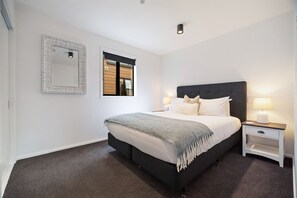 A modern bedroom with a large bed, bedside tables, a mirror, and a window with blinds. - Lake and Mountain Views (Queenstown)