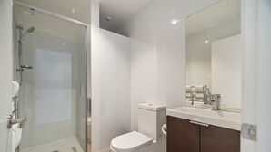 Et moderne badeværelse med brusekabine i glas, et hvidt toilet og en vask med spejl.