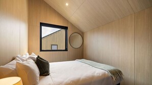 A bedroom with a bed, pillows, a bedside lamp, a round mirror, and a window with a view of a building. - Luxury Queenstown 2Bed Villa (Queenstown)