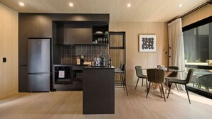 A modern kitchen with a built-in island, dark cabinetry, and a dining area with a glass table and chairs. - Luxury Queenstown 2Bed Villa (Queenstown)