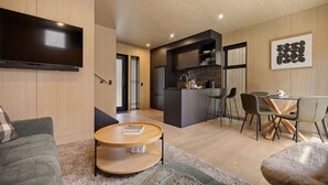 A modern living space with a sofa, a coffee table, a dining area with chairs, a kitchen with a bar, and a flat-screen TV mounted on the wall. - Luxury Queenstown 2Bed Villa (Queenstown)