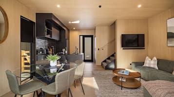 A modern living room with a glass dining table, a sofa, a coffee table, and a staircase leading to another level.