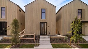 Filare di edifici residenziali moderni in legno, con ingresso centrale, piccoli alberi e cielo sereno.
