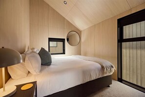 A bedroom with a bed, a round mirror, a bedside lamp, and a window with blinds. - Rākau Villa Queenstown (Queenstown)
