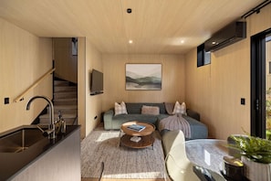 Ein modernes Interieur mit einer Treppe, einer Sofagarnitur, einem Couchtisch und einem an der Wand befestigten Flachbildfernseher.