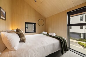 A modern bedroom with a large bed, a window, and a view of the outside. - Kowhai Luxury Villa Queenstown (Queenstown)
