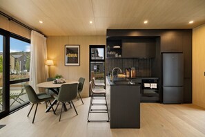 A modern kitchen with a central island, a dining area with chairs, and a view of the outside. - Kowhai Luxury Villa Queenstown (Queenstown)